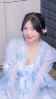 Charming portrait of a young woman in a light blue dress with delicate details, smiling indoors.